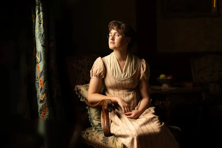 A young lady wearing a 19th Century night gown, looking out the window