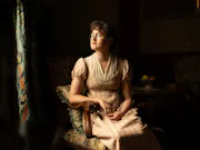 A young lady wearing a 19th Century night gown, looking out the window