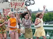 A group of white women in 60's attire holding up protest signs and laughing