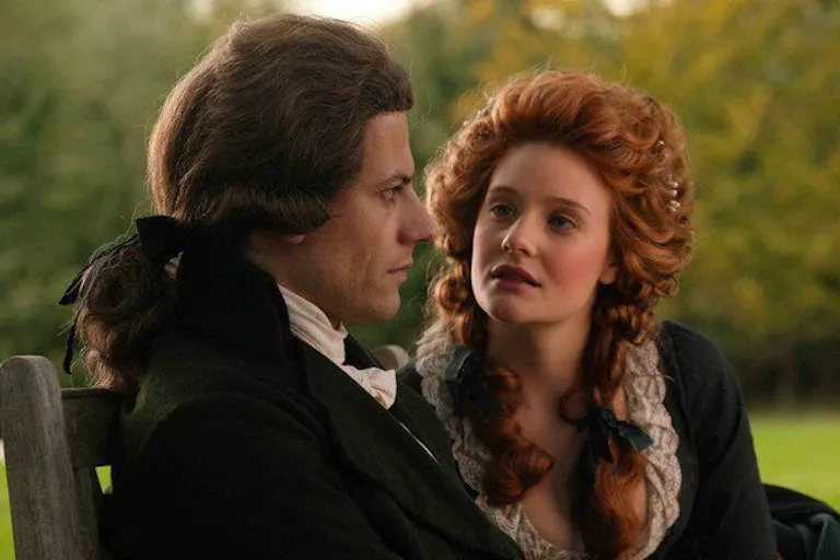A woman and man sitting on a park bench, dressed in 18th Century attire