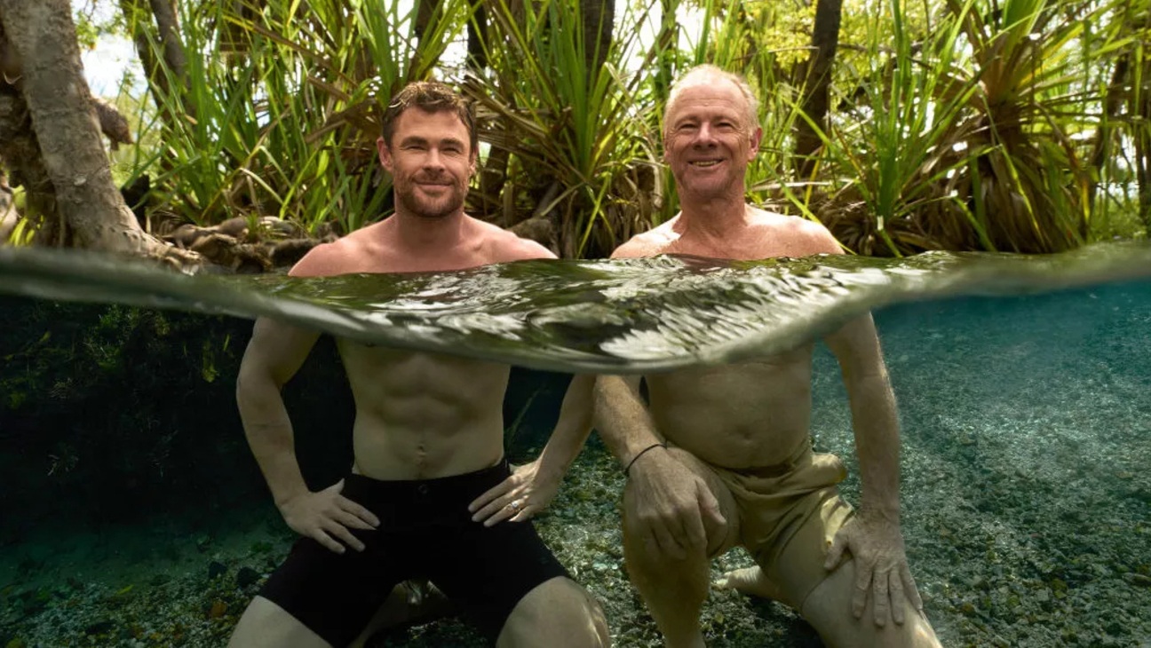 Two white men (one middle aged, one elderly) swimming in a body of water in a rainforest