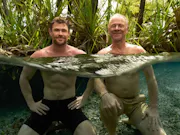 Two white men (one middle aged, one elderly) swimming in a body of water in a rainforest