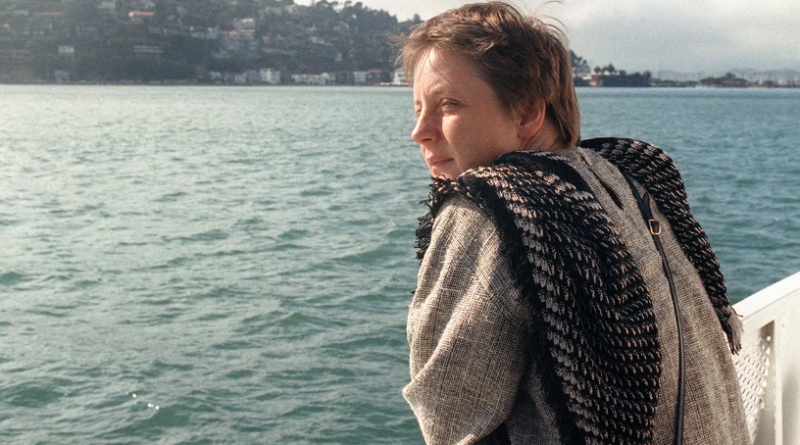 A white woman leaning on a railing looking out onto the blue sea