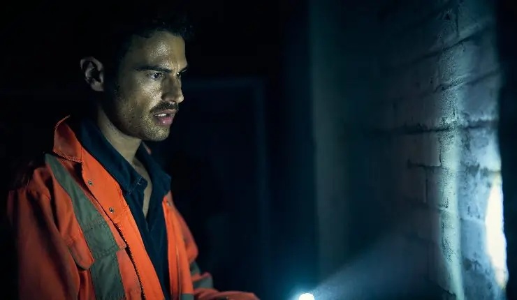 A white man wearing a high-vis jacket in a dark room, pointing a torchlight at a wall