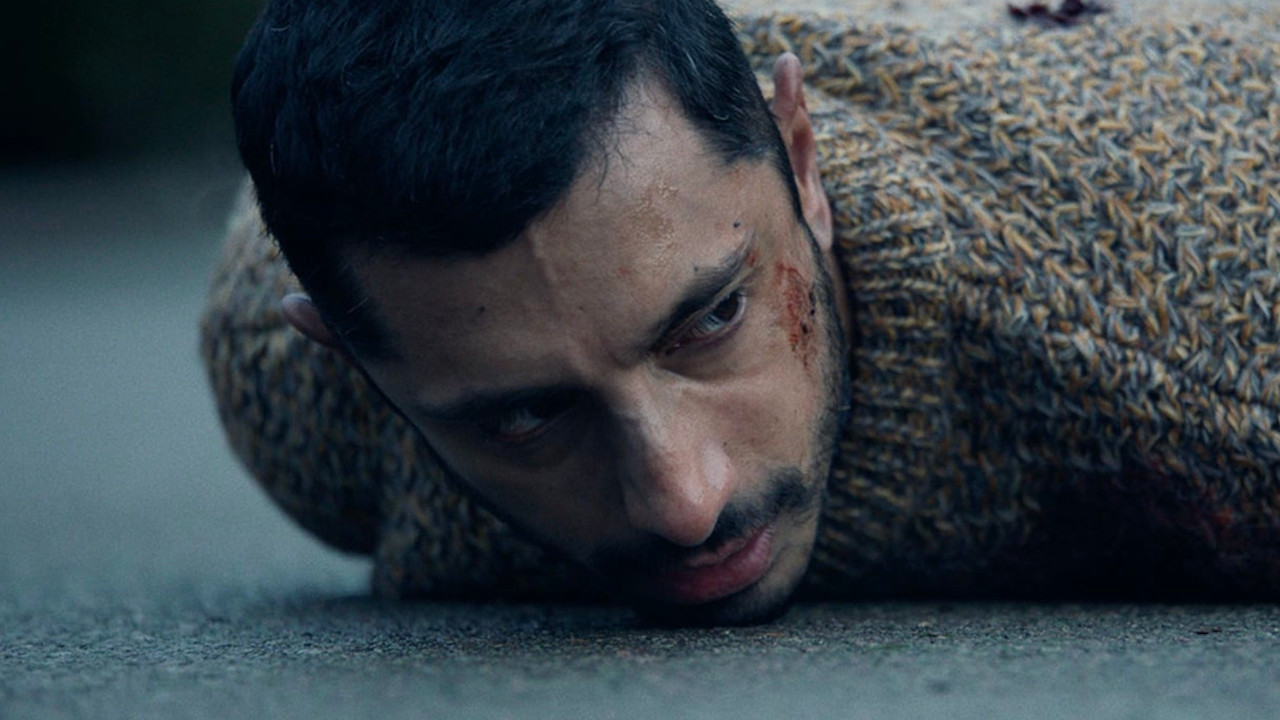 A close up of a south asian young man laying face-down on concrete, with blood on his cheek
