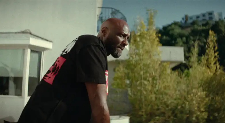 A black man in a black t shirt leaning on a balcony and looking out over it