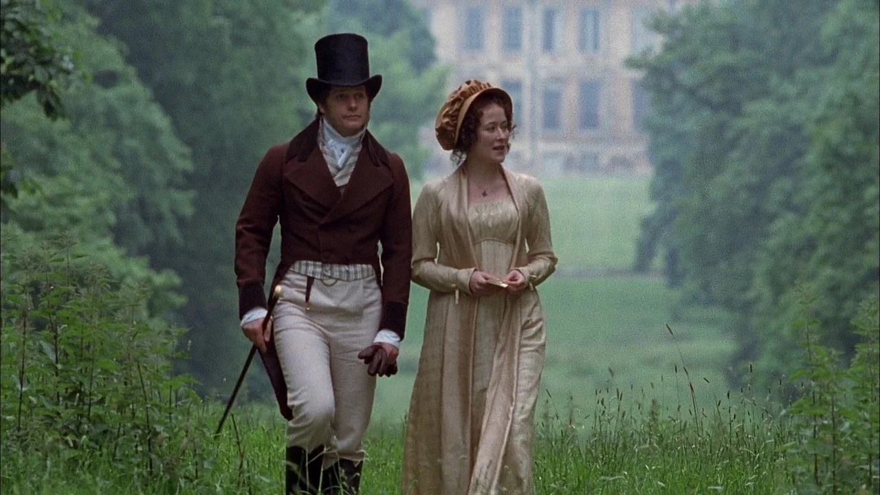 A woman and man dressed in period attire walking in a grassy area
