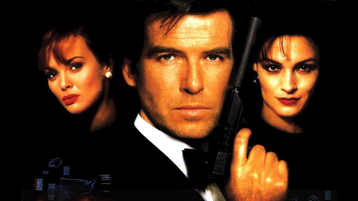 A suited white man with a serious face, holding a gun with two women either side of him. All of which are shrouded by darkness, with light only on their faces