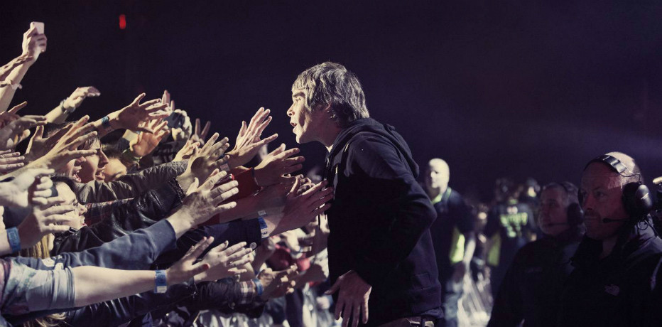 A white man in a black hoodie facing dozens of hands stretched out towards him