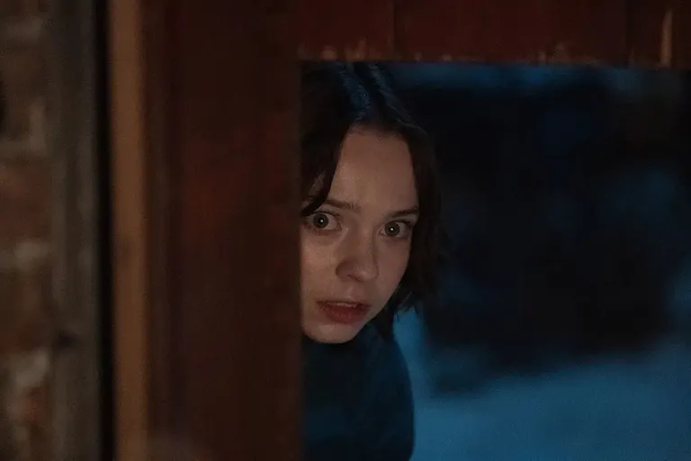 A young brown-haired caucasian woman peeking from around a corner, with a scared face