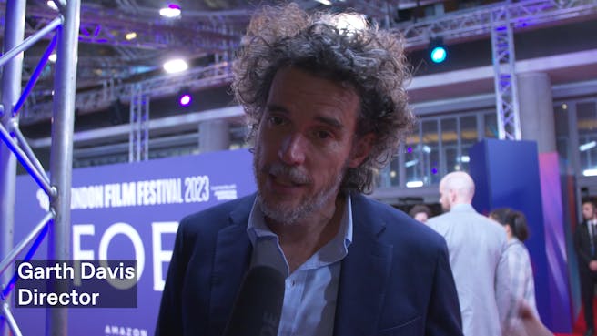 A white man with dark hair and grey beard talking into a microphone on the red carpet