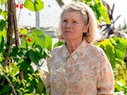 An older white woman in a floral shirt stands in a sunny garden