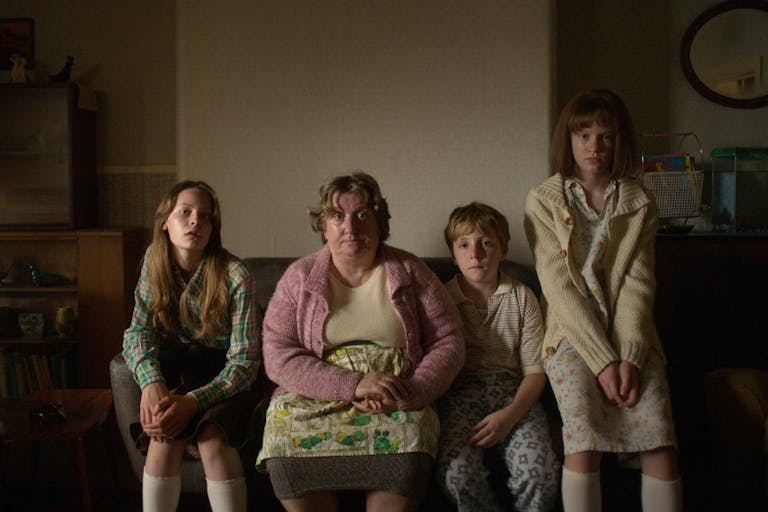A white working class family in the 1970s sitting on a sofa in their muted house