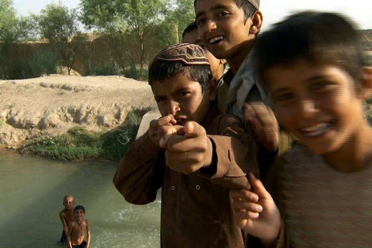 Close up, playful shot of smiling young Afgani boys playing in and around a river