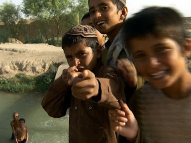 Close up, playful shot of smiling young Afgani boys playing in and around a river 