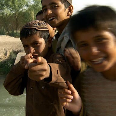 Close up, playful shot of smiling young Afgani boys playing in and around a river 