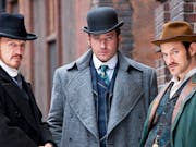 Three men in smart period business clothes and hats staring seriously at the audience