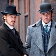 Three men in smart period business clothes and hats staring seriously at the audience