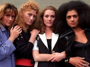 Three white women and one Black woman stand with their arms linked and around each other