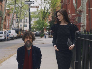 A brunette white woman and a dark haired with greys white man walk down a street
