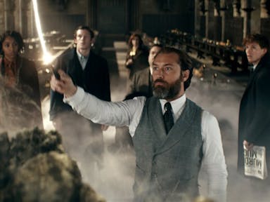A white man in a suit holding aloft a wand with white stream of light coming out of it, surrounded by others