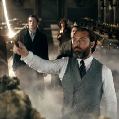 A white man in a suit holding aloft a wand with white stream of light coming out of it, surrounded by others