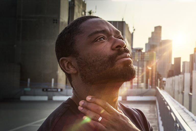 A Black man looks up to the sky with light across his face in contemplation
