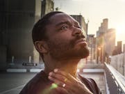 A Black man looks up to the sky with light across his face in contemplation