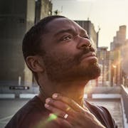 A Black man looks up to the sky with light across his face in contemplation