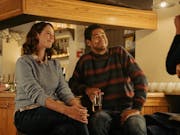 A young white woman and a young Black man wearing jumpers sitting at the bar or a pub looking polite