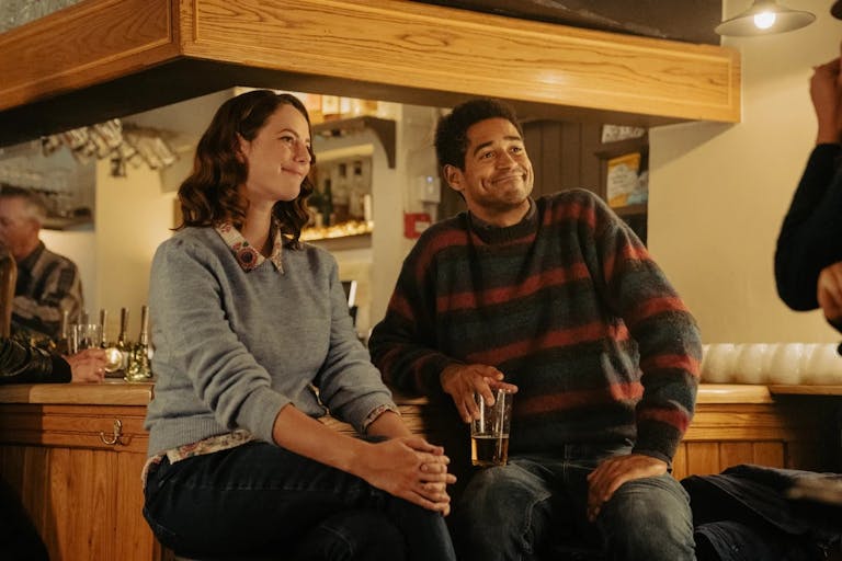 A young white woman and a young Black man wearing jumpers sitting at the bar or a pub looking polite 