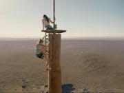 Two women climb on top of an abandoned radio tower.