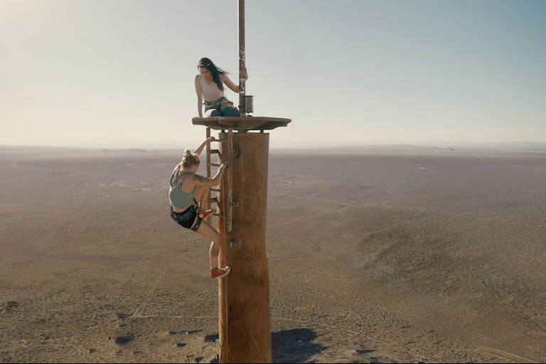Two women climb on top of an abandoned radio tower.