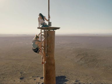Two women climb on top of an abandoned radio tower.