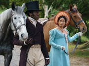 A man and a woman in period costume walking side by side while guiding their horses by the reins