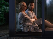 Blonde older woman sits beside a young man leant against a window at night