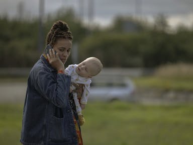 A young Black woman holding a white baby while she's on the phone walking outside