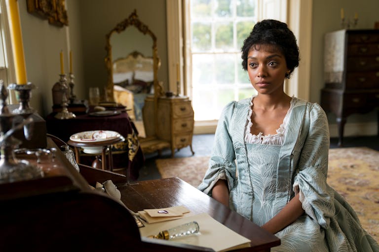 Young woman in a blue old-fashioned dress sits at a desk
