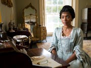 Young woman in a blue old-fashioned dress sits at a desk