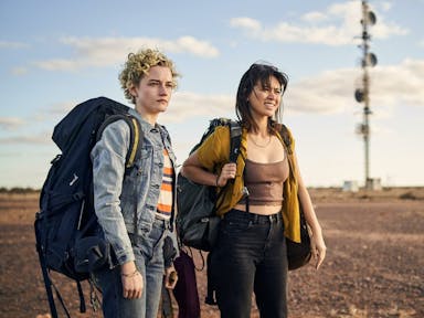 Two young white women with large backpacks in a dusty, sandy landscape 