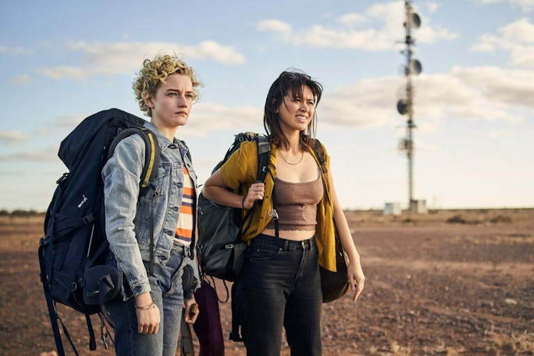 Two young white women with large backpacks in a dusty, sandy landscape 