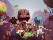Animated video game image of a knitted creature flying through the air, smiling, with hot air balloons all around him in the sky.