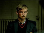 Blonde adolescent boy in a dark school uniform, his face covered in blood.