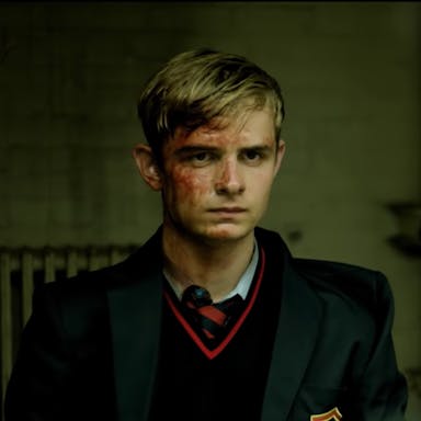 Blonde adolescent boy in a dark school uniform, his face covered in blood. 