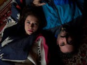 A young man and woman are lying on their backs on a carpet, looking upwards at the camera.