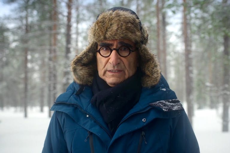 Man in furry hat and glasses looks at the camera against a snowy backdrop