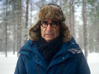 Man in furry hat and glasses looks at the camera against a snowy backdrop