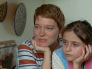 Woman with cropped blonde hair and young girl with brown hair sit side by side cupping their chins in their hands.