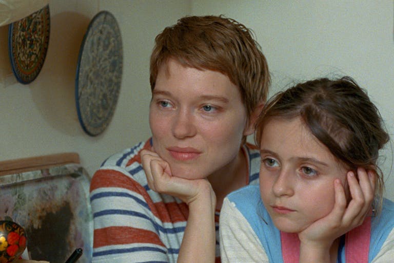 Woman with cropped blonde hair and young girl with brown hair sit side by side cupping their chins in their hands. 