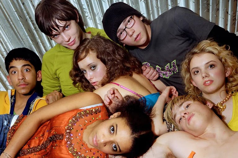 A group of young people tangled up and laying on top of each other looking at the camera
